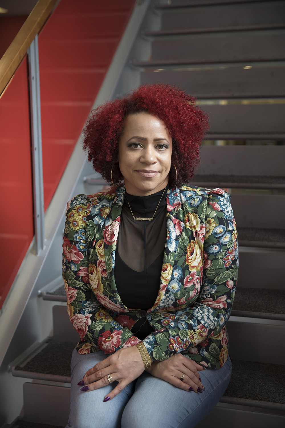 Nikole Hannah-Jones looking at the camera, wearing a floral blazer, sitting on a staircase
